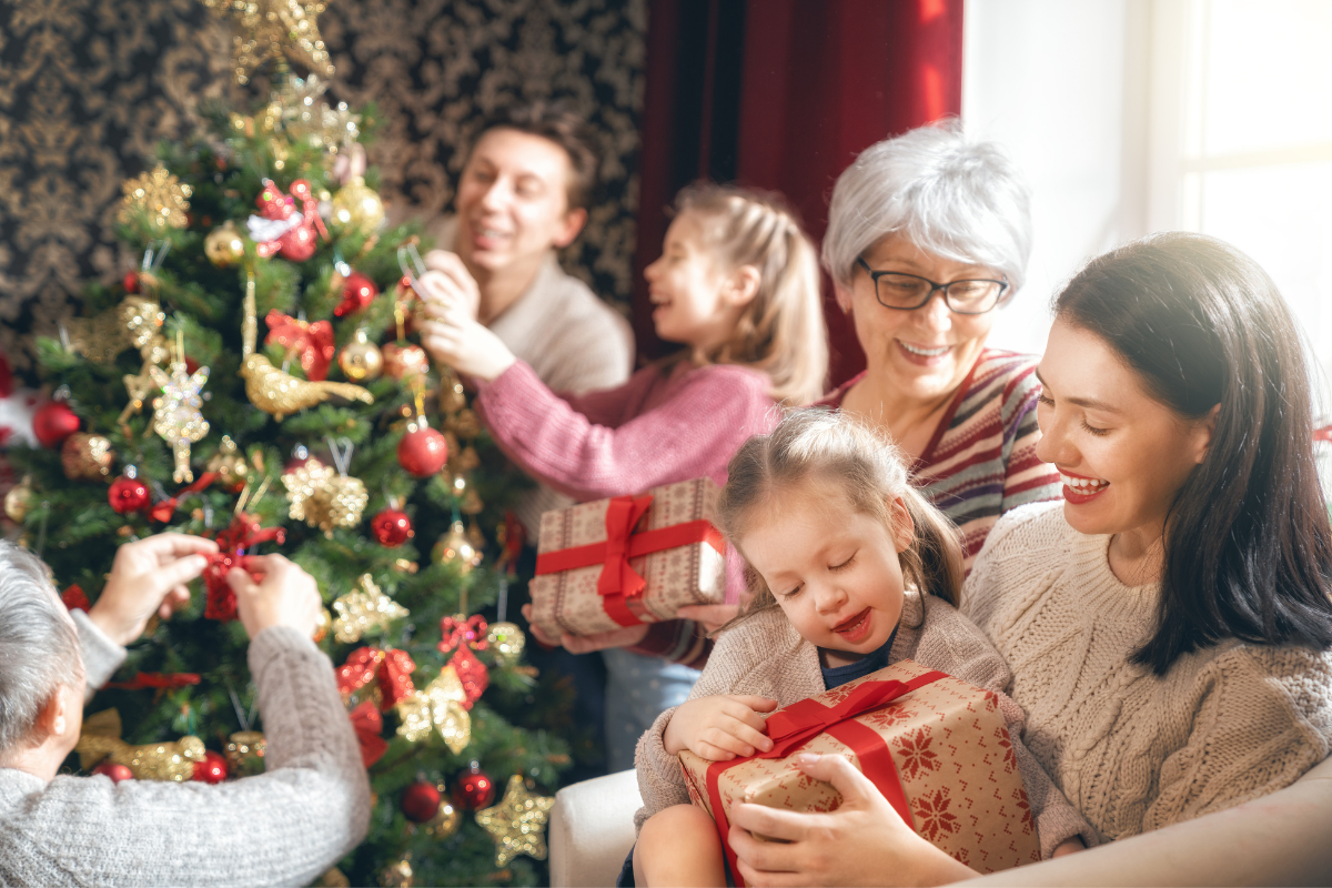 Last Minute Weihnachtsgeschenke für Kinder_Familie sitzt vor Weihnachtsbaum und tauscht Weihnachtsgeschenke aus